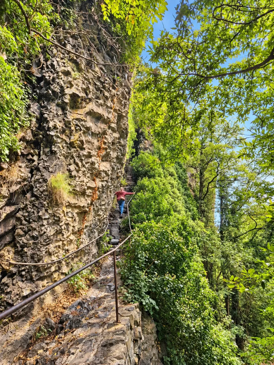 Personne montant un escalier taillé dans la roche, une main courante le long de la paroi
