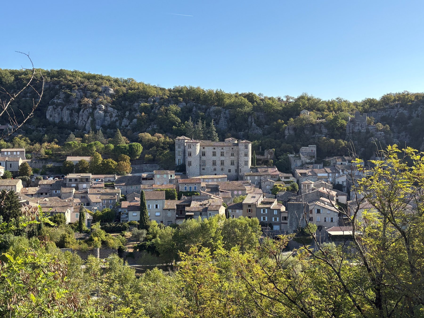 Le château de Vogüé au-dessus des toits du village, adossé à la falaise boisée