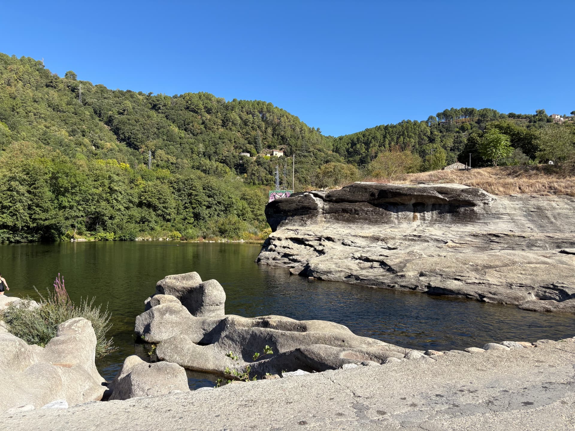 Grand bassin d'eau calme du Chassezac entre les rochers, collines boisées à l'arrière-plan