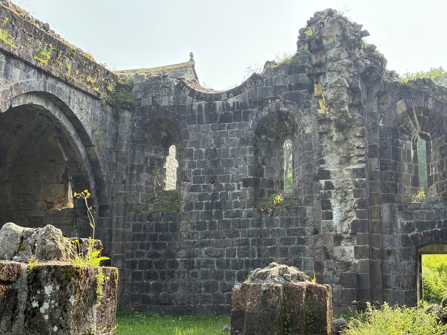 Mur intérieur en pierre de l'abbaye avec grand arc, baies en plein cintre et bases de piliers couvertes de lichen