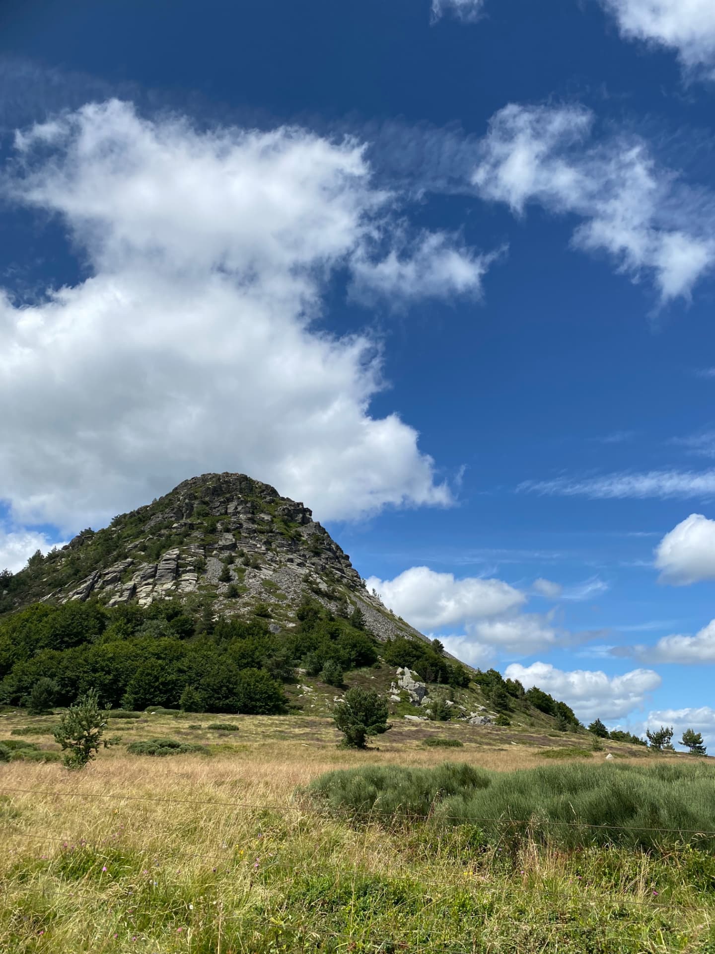 Cône rocheux du Mont Gerbier-de-Jonc au-dessus d'une ceinture de forêt, sous un ciel bleu profond et de grands nuages blancs