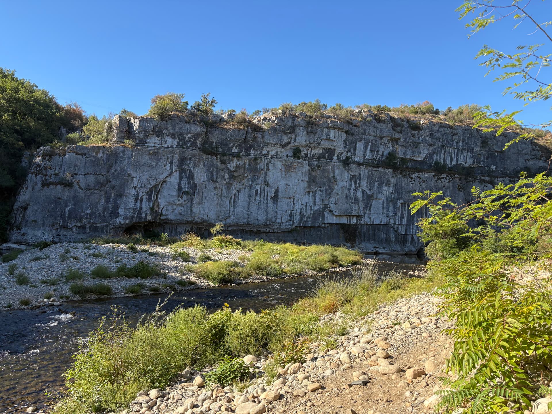 Le Chassezac longeant une haute falaise calcaire sous un ciel bleu