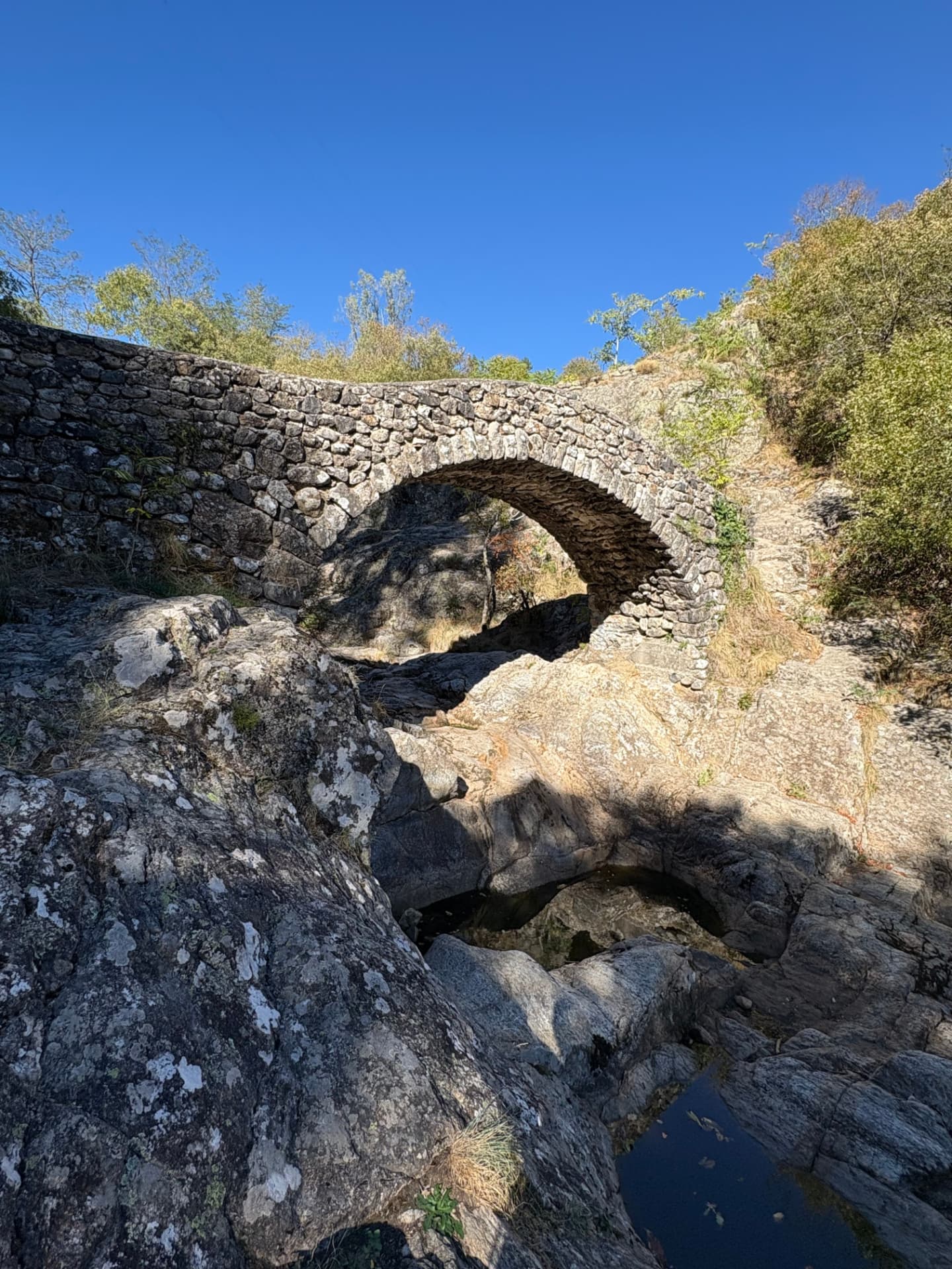 Pont de pierre à une arche au-dessus de rochers et de petites vasques d’eau, sous un ciel bleu