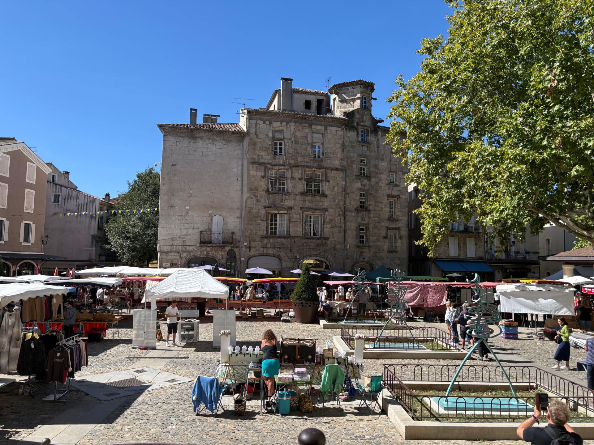 Place pavée avec étals blancs et rouges devant une haute façade ancienne en pierre
