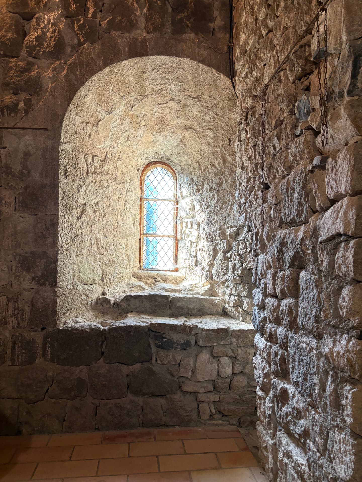 Baie voûtée et murs de pierre à l'intérieur du château de Ventadour, éclairés par une fenêtre à vitrail losangé