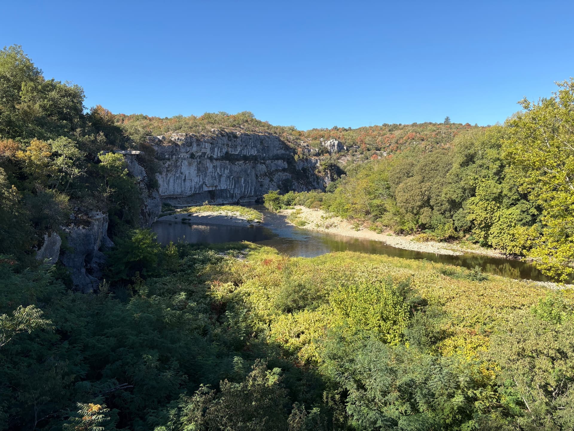 Vue large du Chassezac depuis les hauteurs : falaise calcaire, plage de galets et versants boisés