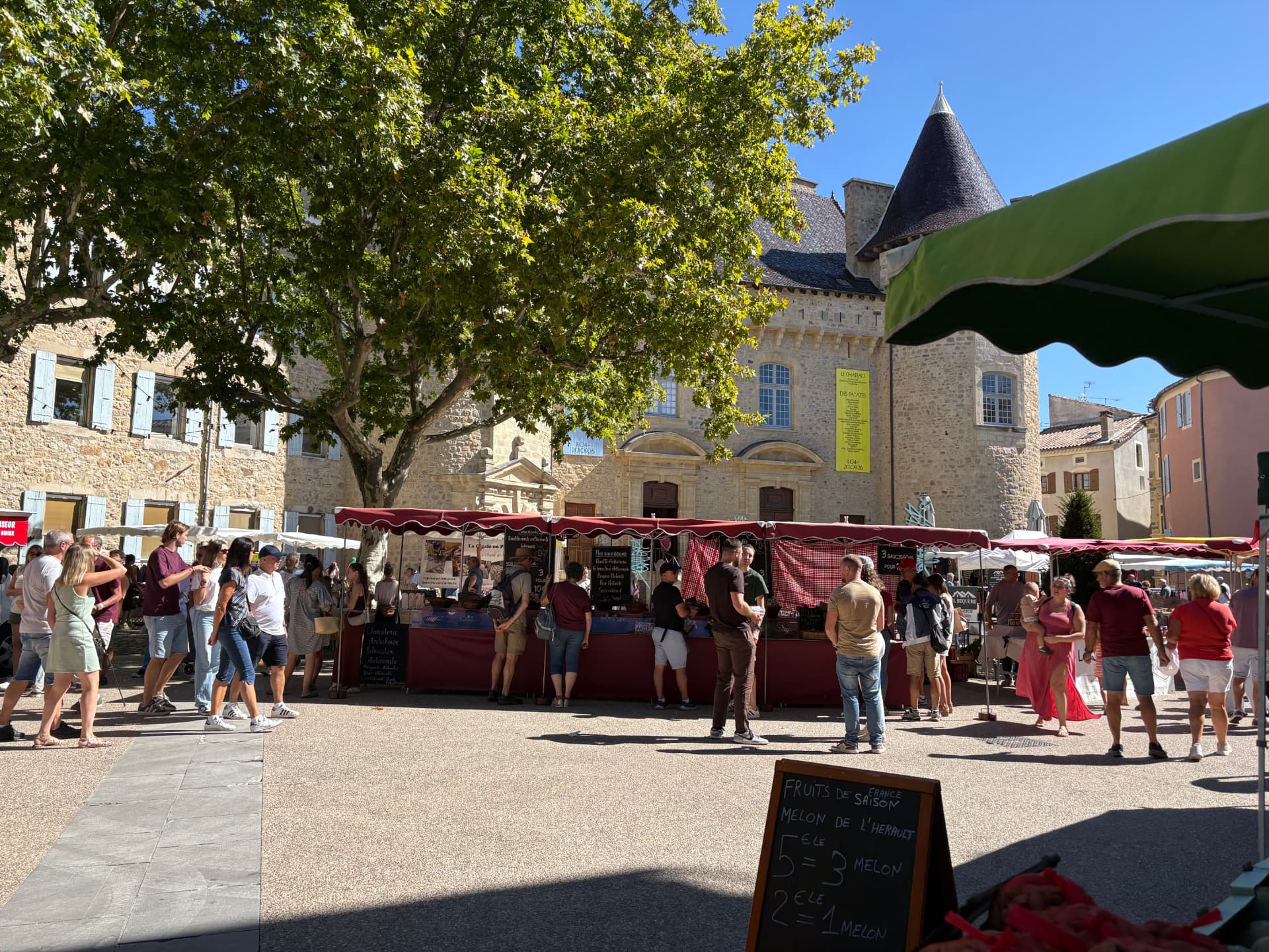 Longue rangée d'étals aux auvents rouges devant la façade du château, promeneurs sur la place