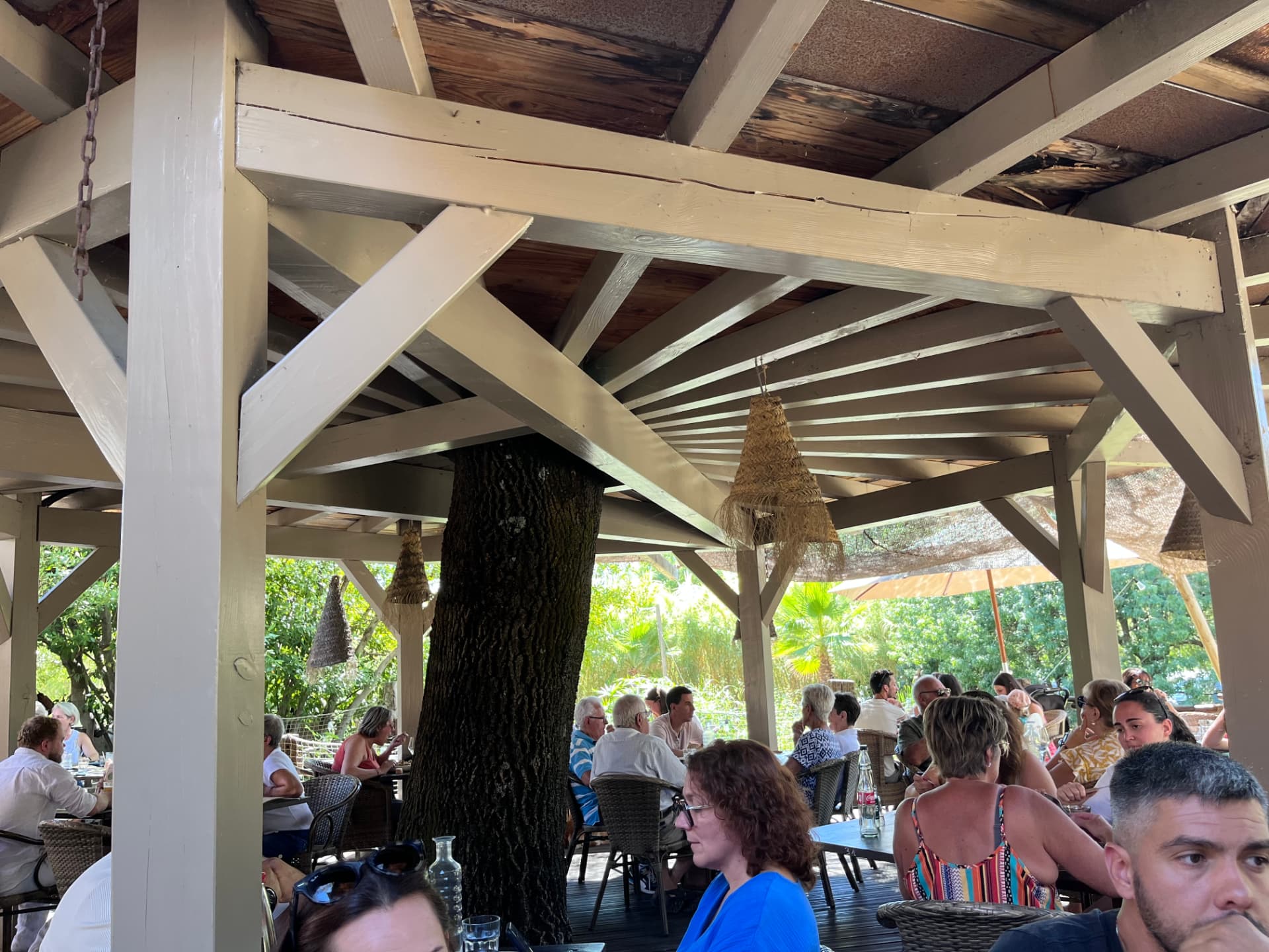 Ambiance de service sous la charpente de la terrasse couverte de Coquerie, tables occupées autour d'un arbre