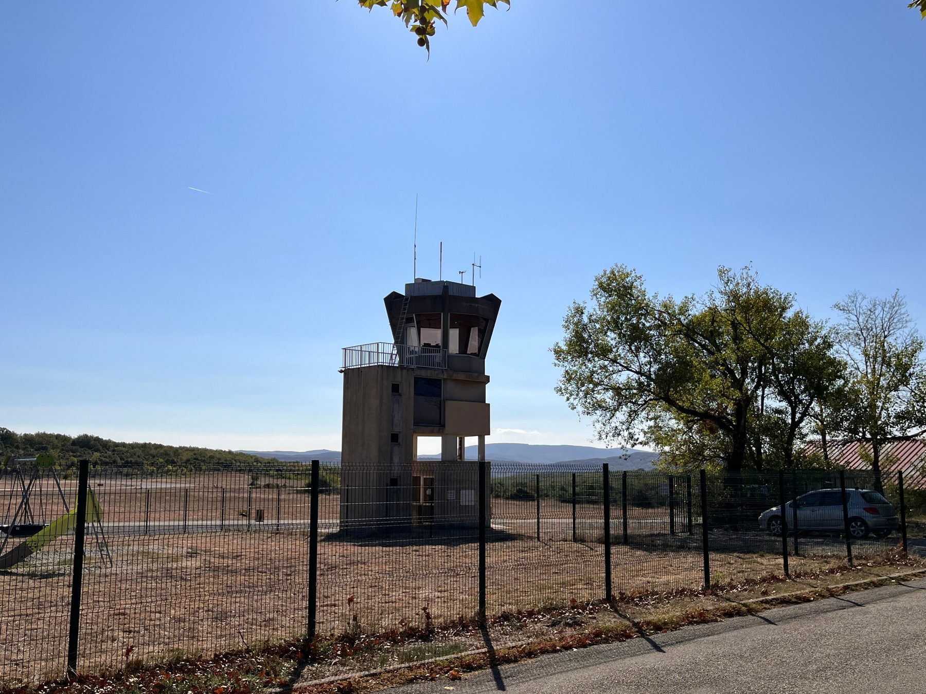Tour de contrôle de l'aérodrome vue depuis la route, derrière la clôture, avec les collines à l'horizon