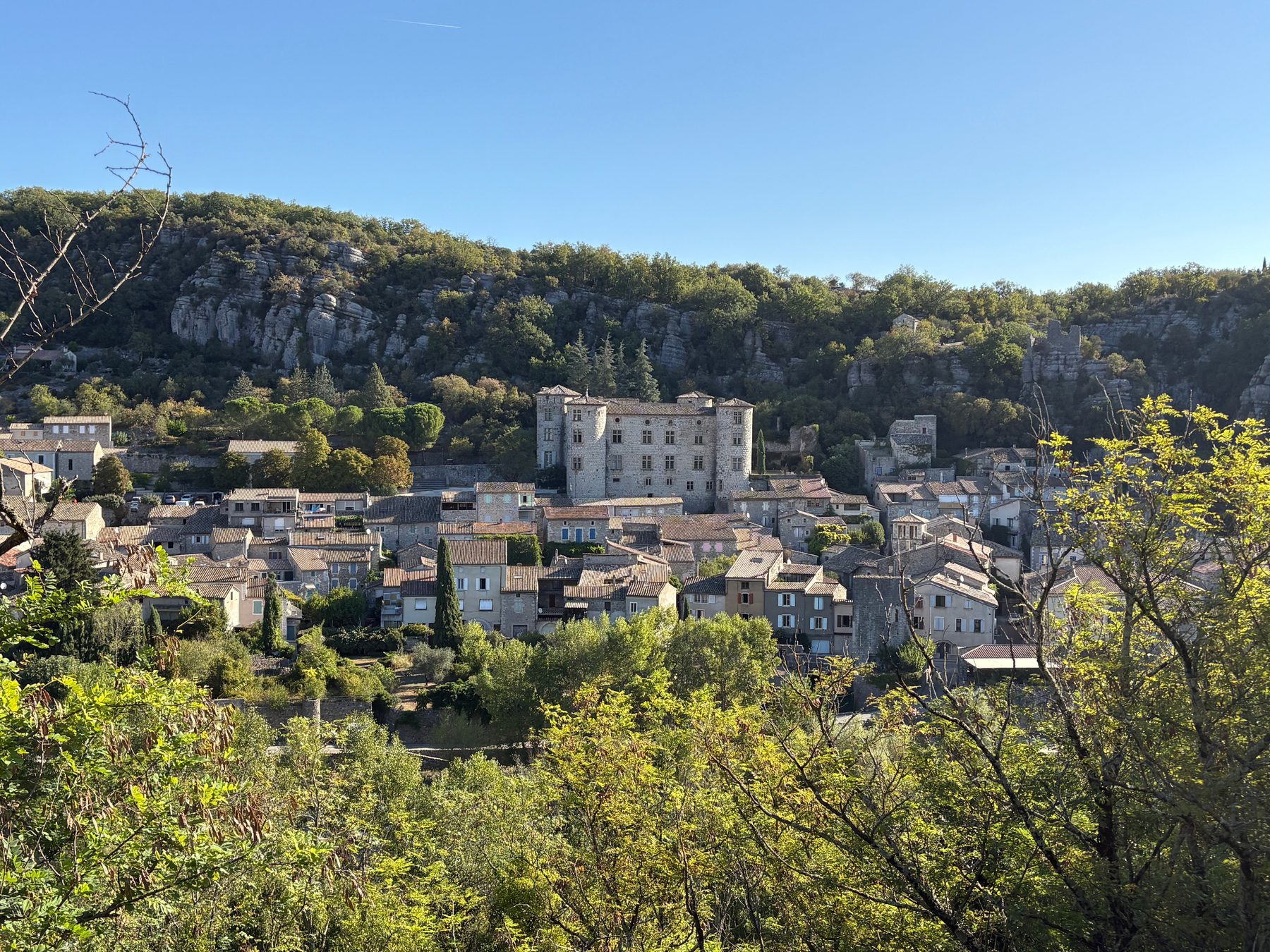 Village de Vogüé en amphithéâtre au pied de la falaise, château au centre des toits de tuiles