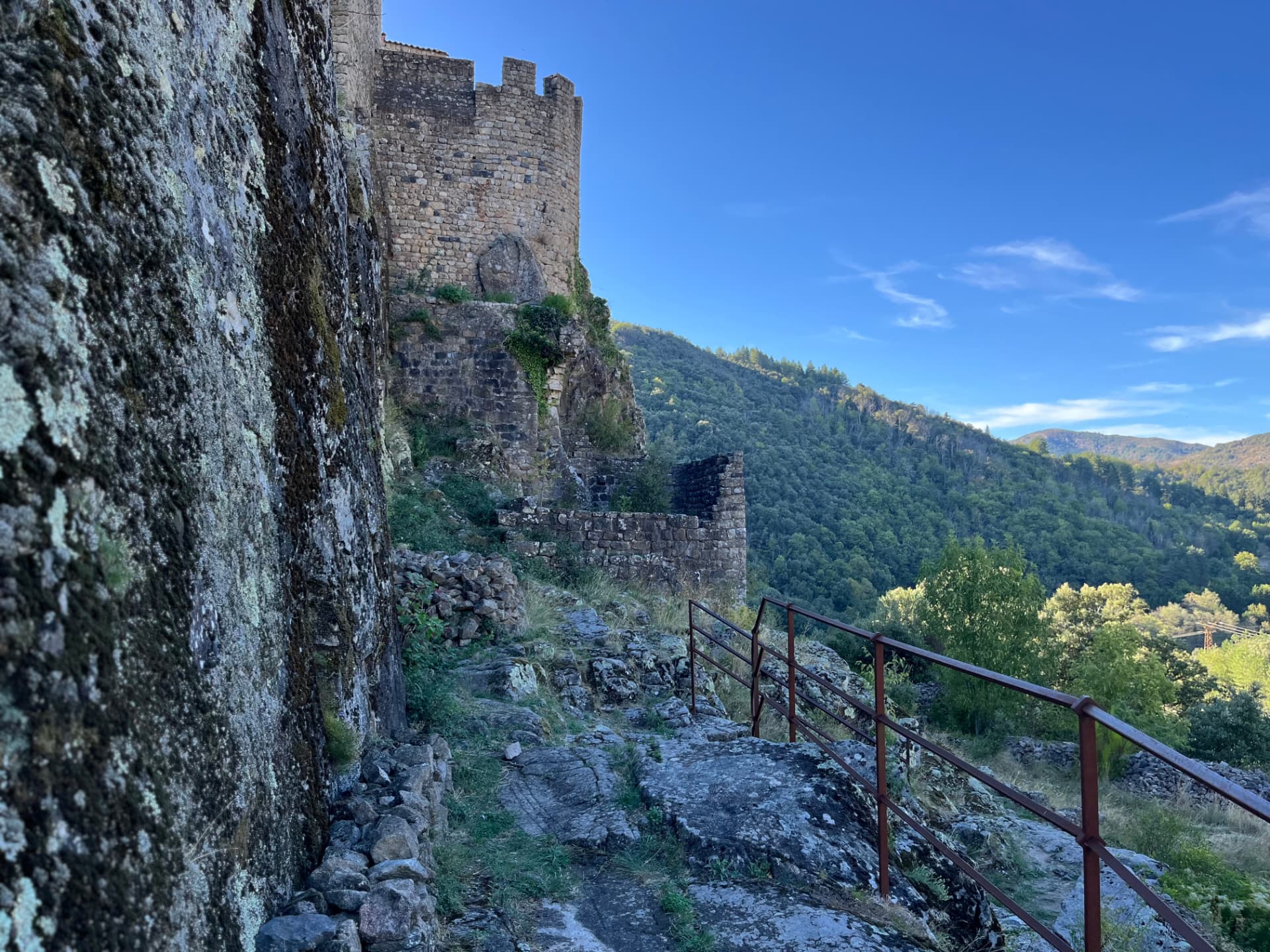 Sentier longeant la muraille du château de Ventadour, avec la tour ronde et la vallée boisée
