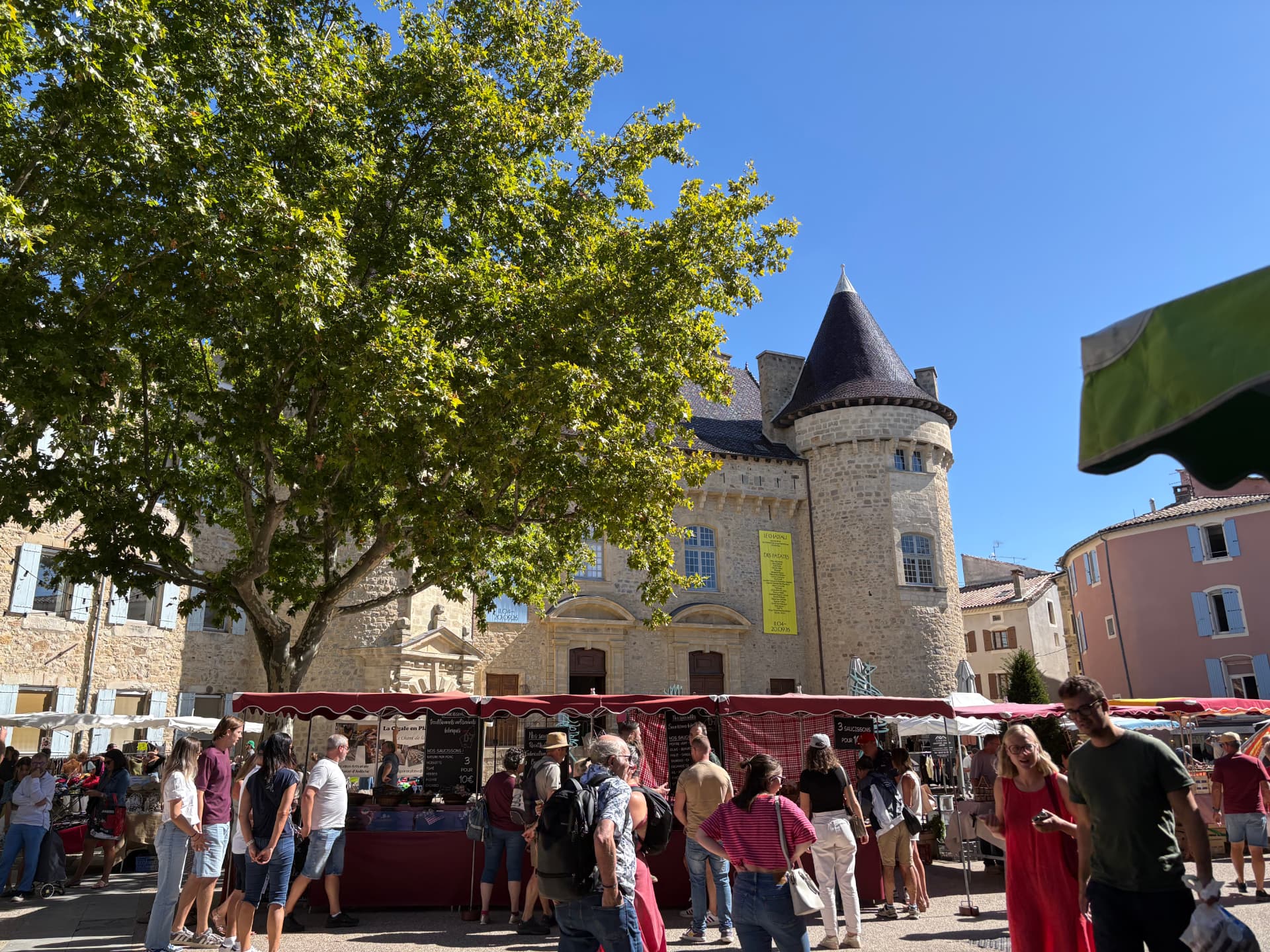 Grand platane et foule du marché devant le château et sa tour à toit conique