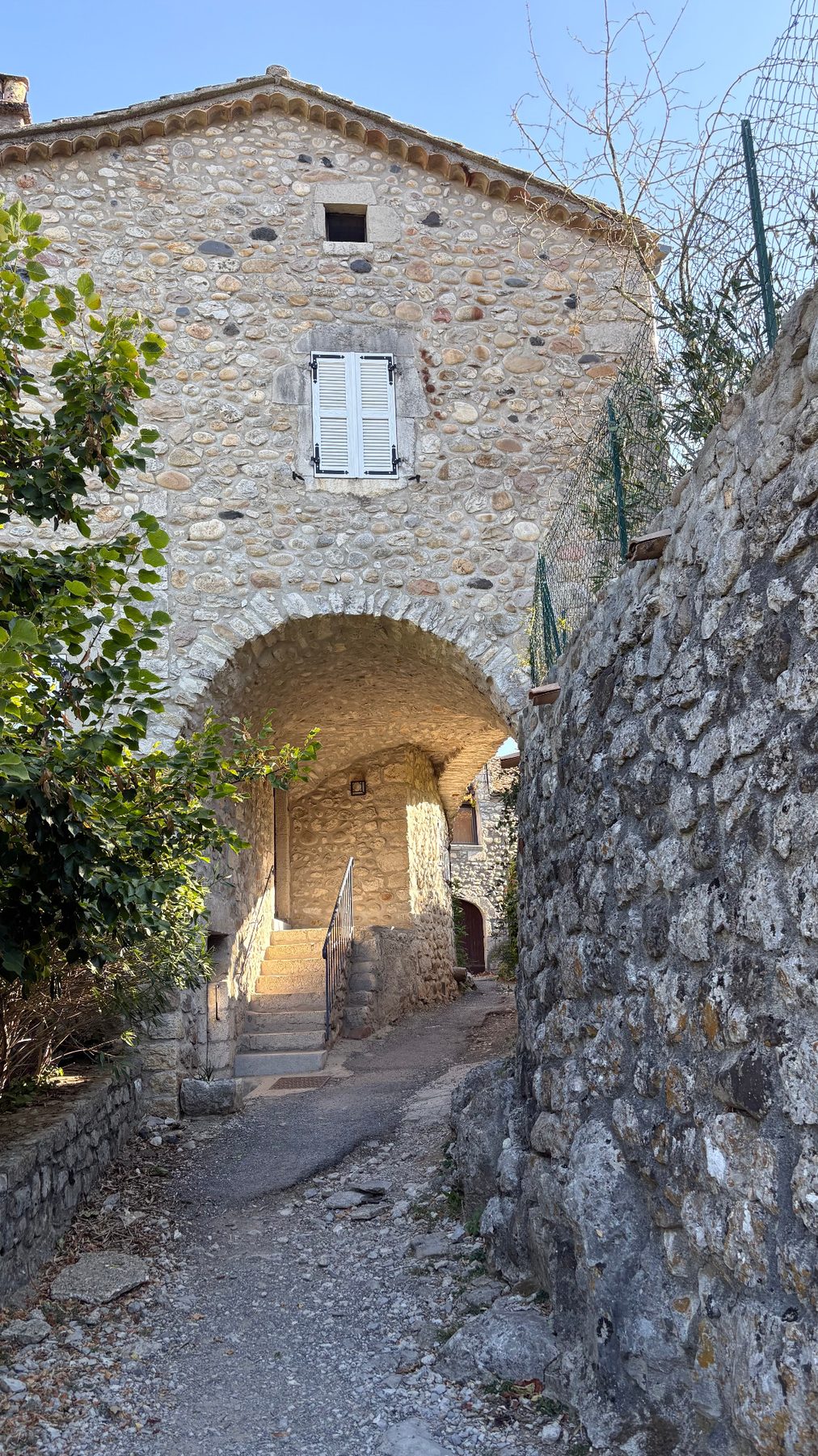 Ruelle empierrée passant sous une maison ancienne, arche voûtée et escalier dans le vieux village