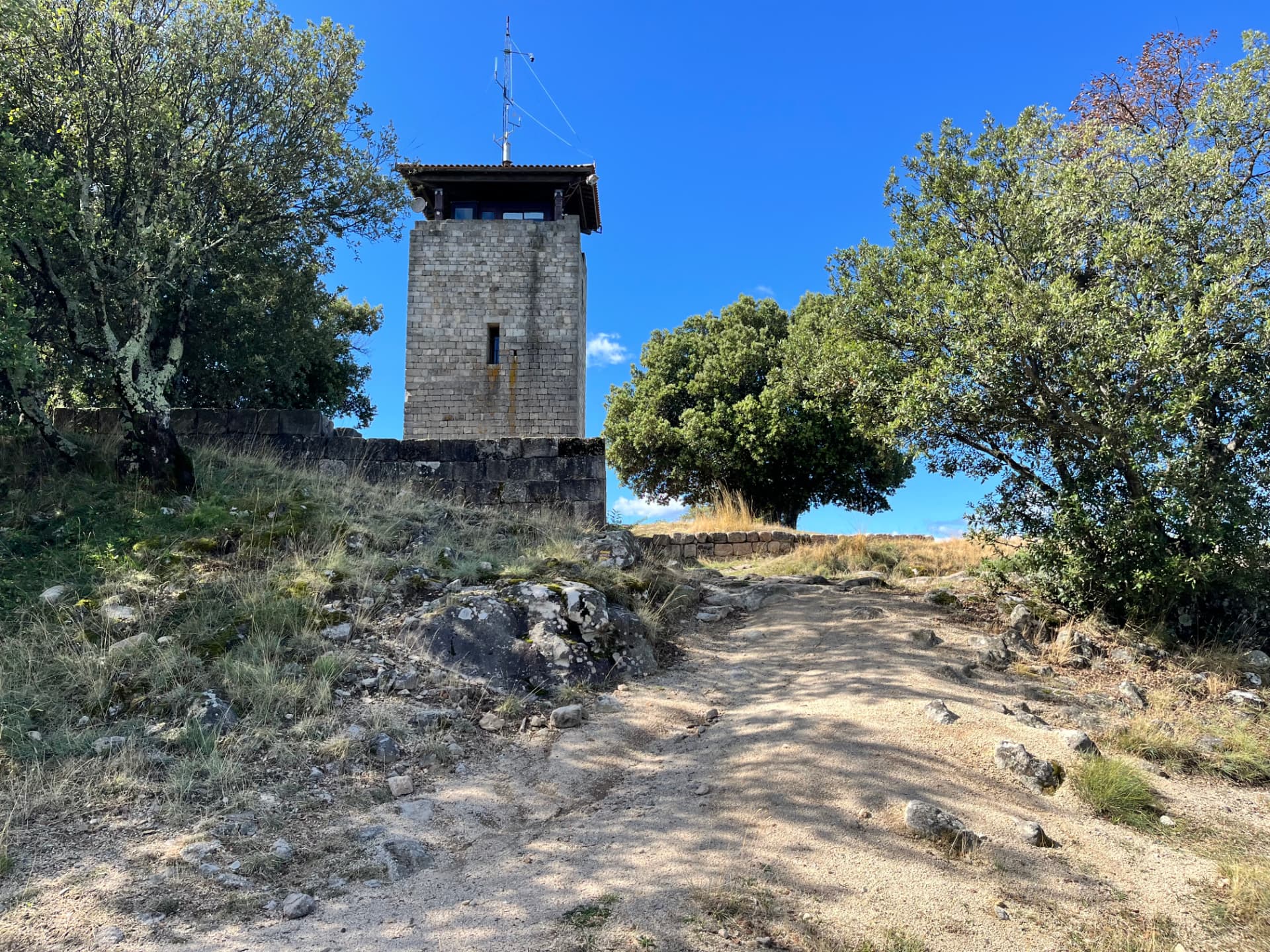 Tour de Brison au bout d'un chemin de terre, entre des arbres et un muret de pierre, sous un ciel bleu