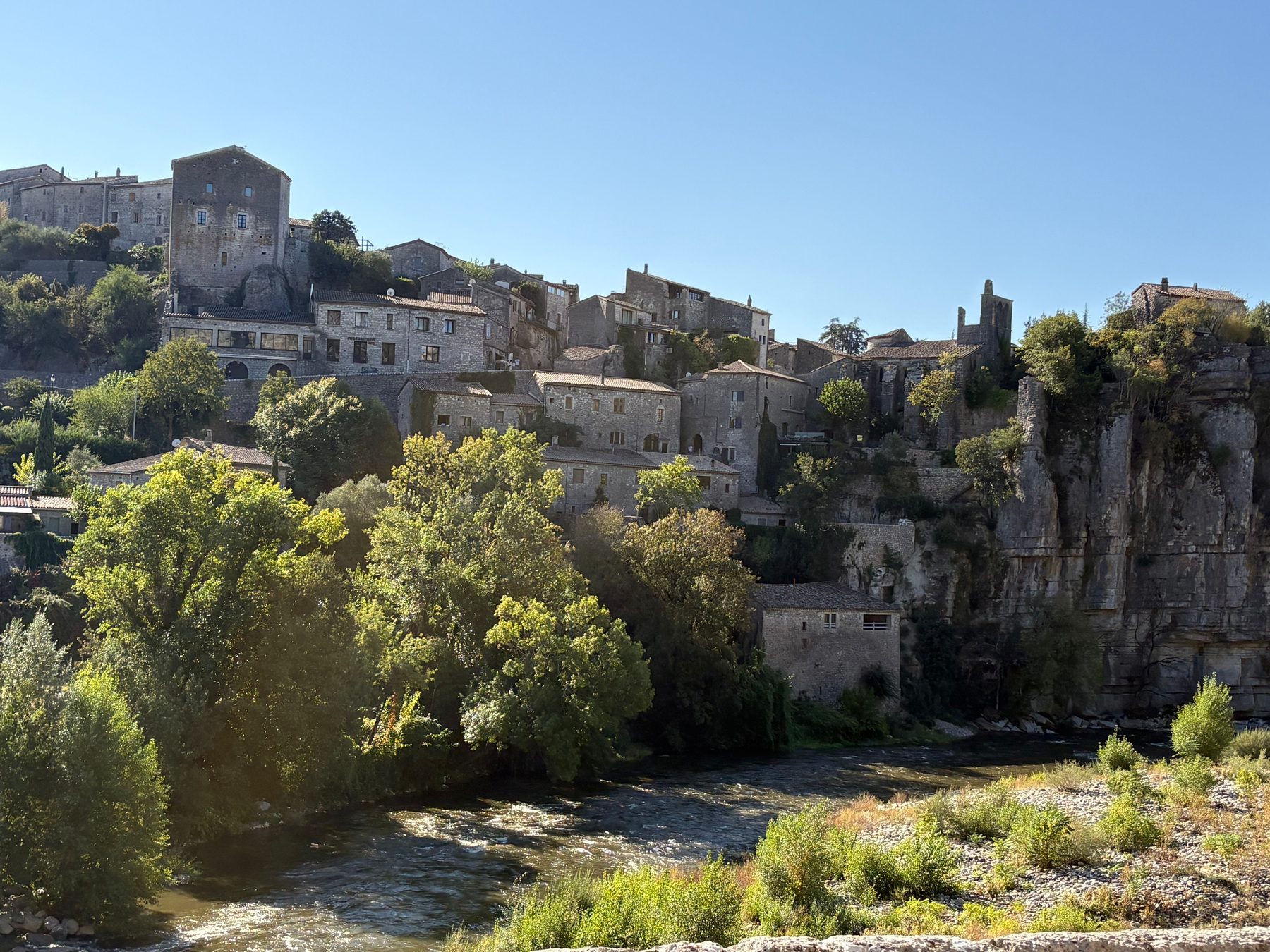 Village de Balazuc accroché à la falaise calcaire au-dessus de l'Ardèche, maisons de pierre étagées et rivière au premier plan