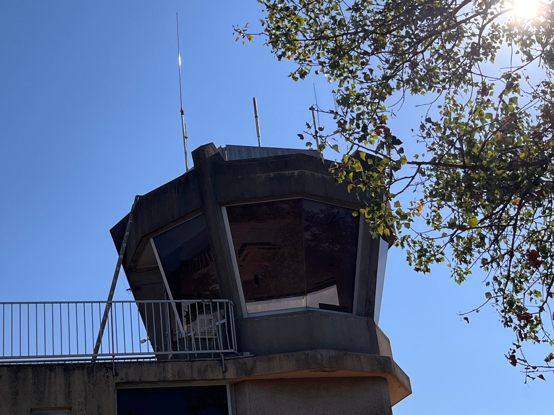 Détail de la vigie vitrée de la tour de contrôle et de ses antennes, sous les branches d'un arbre