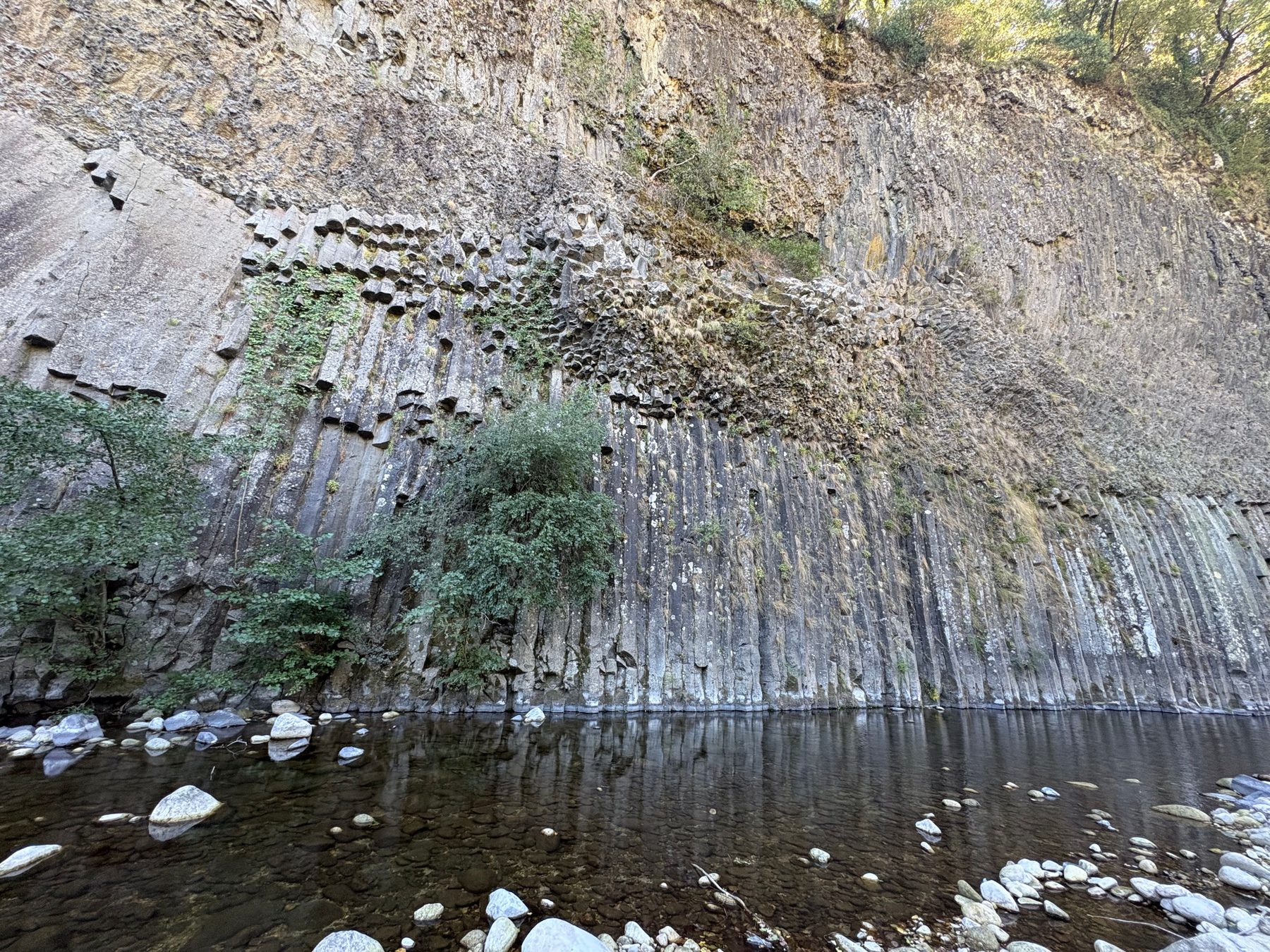 Longue paroi de prismes basaltiques reflétée dans l’eau calme de la rivière