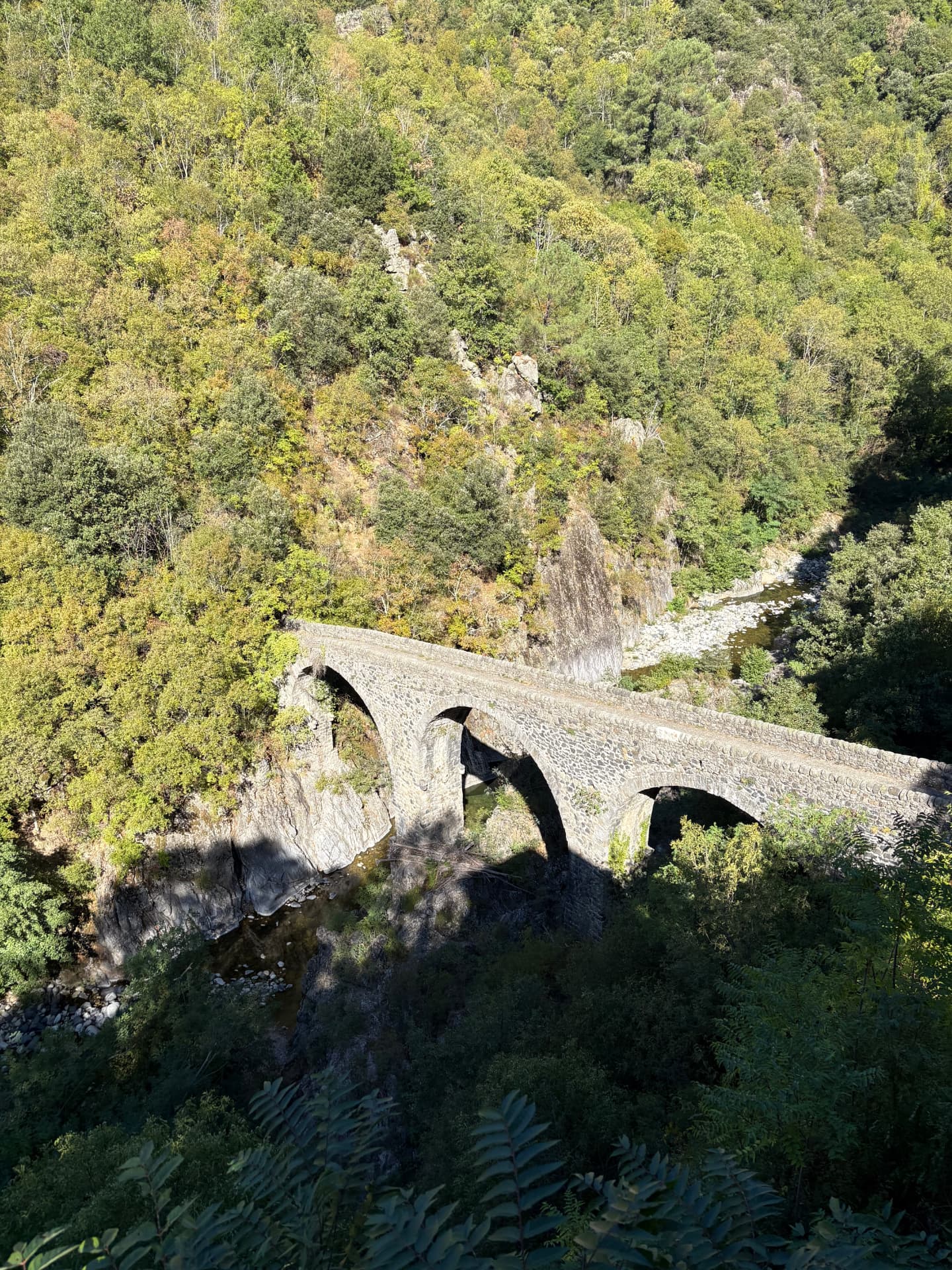Vue d’en haut sur un pont de pierre à trois arches enjambant une rivière au fond d’une gorge boisée