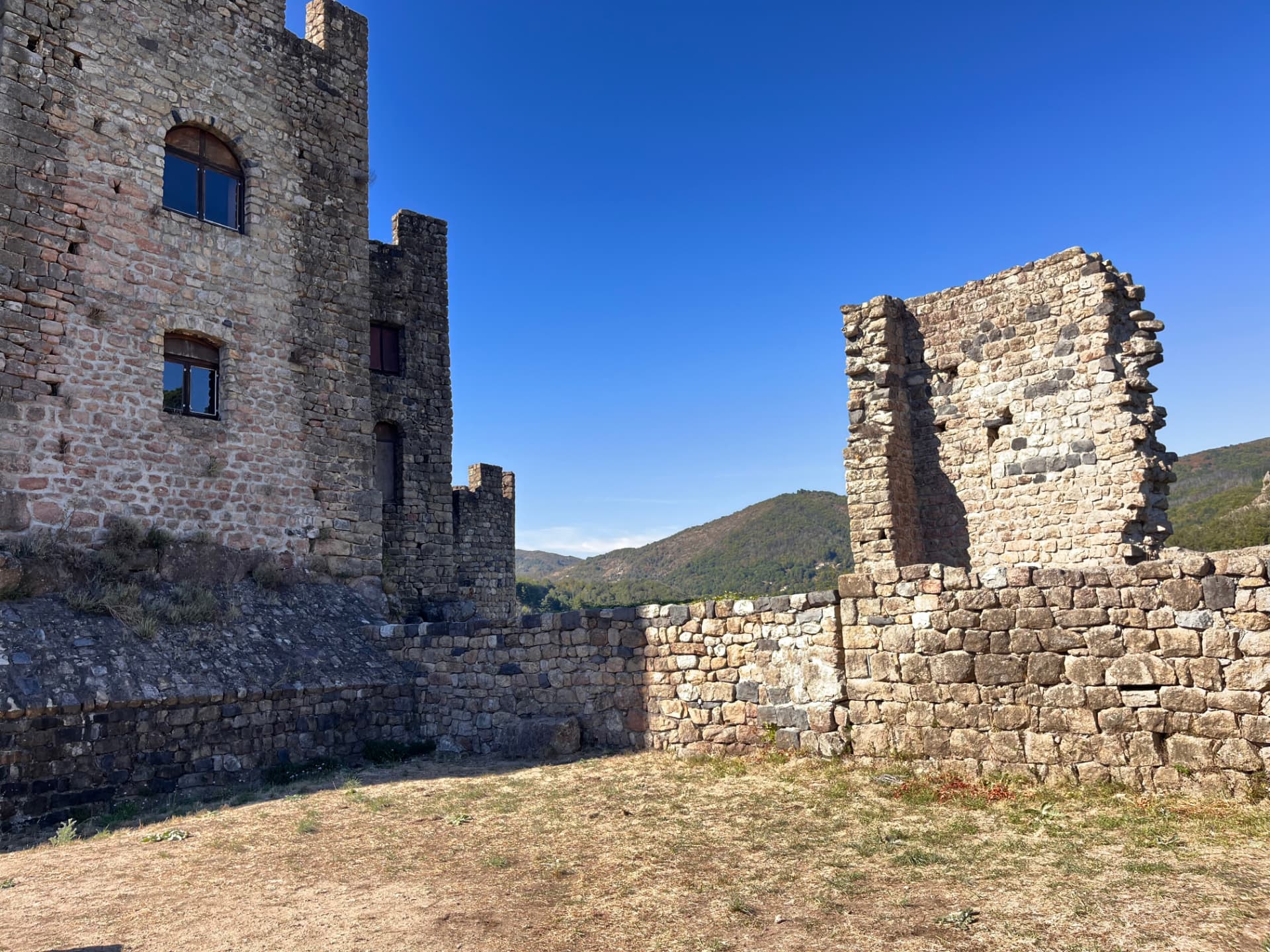 Cour et vestiges du château de Ventadour ouverts sur les reliefs boisés de la vallée