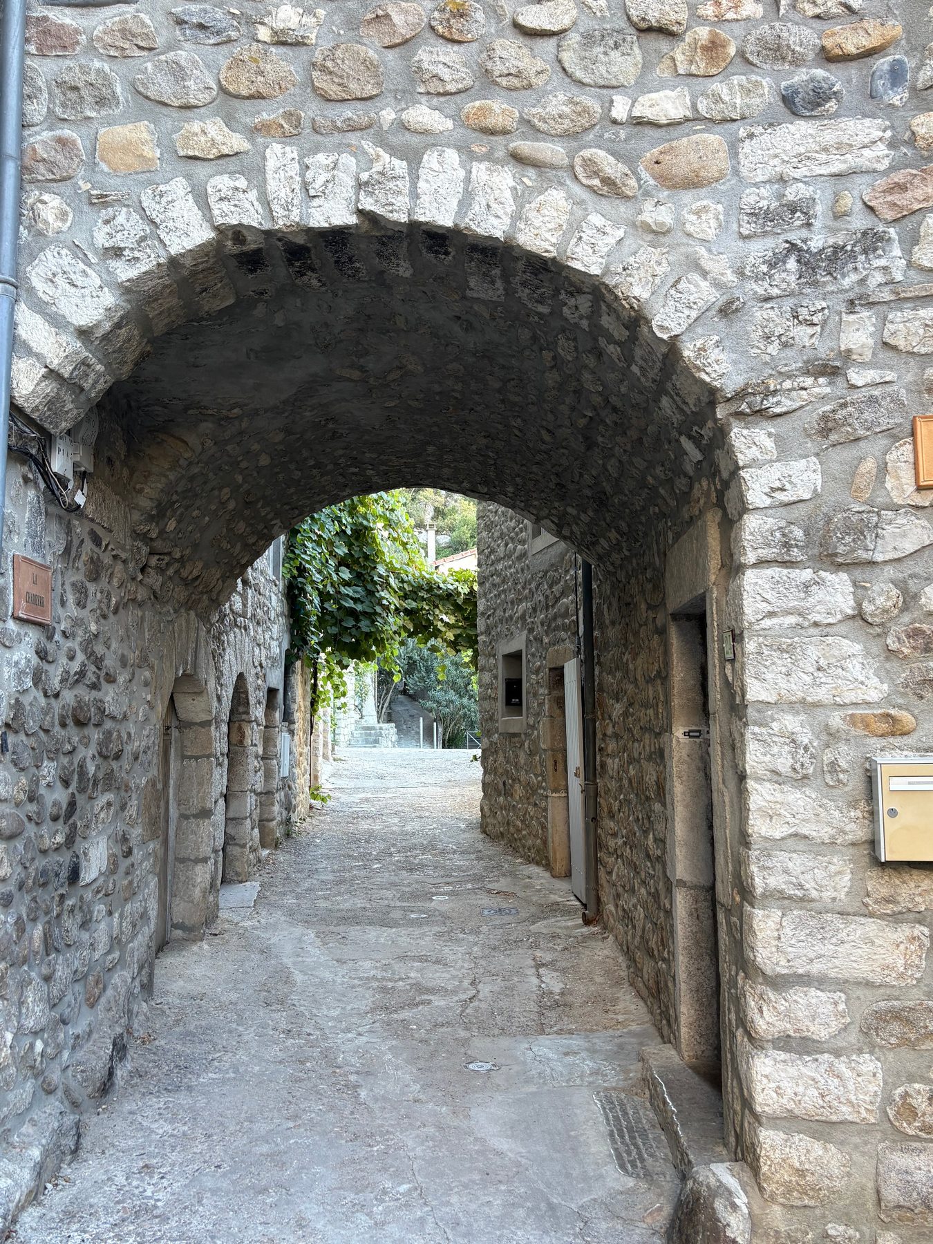 Passage voûté en pierre dans le vieux village de Vogüé, ouvrant sur une treille