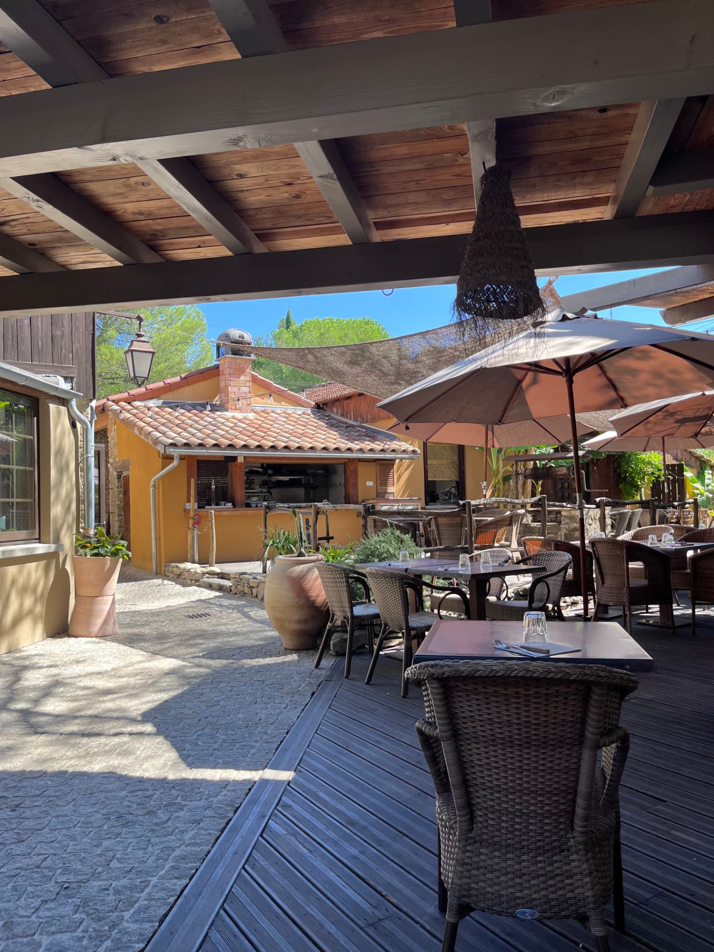 Terrasse en bois de Coquerie sous pergola, face à la cuisine extérieure au toit de tuiles