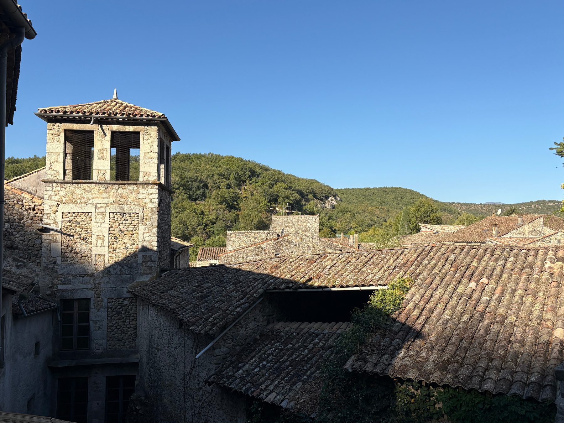 Clocher-mur de pierre et toits de tuiles de Vogüé devant les collines boisées