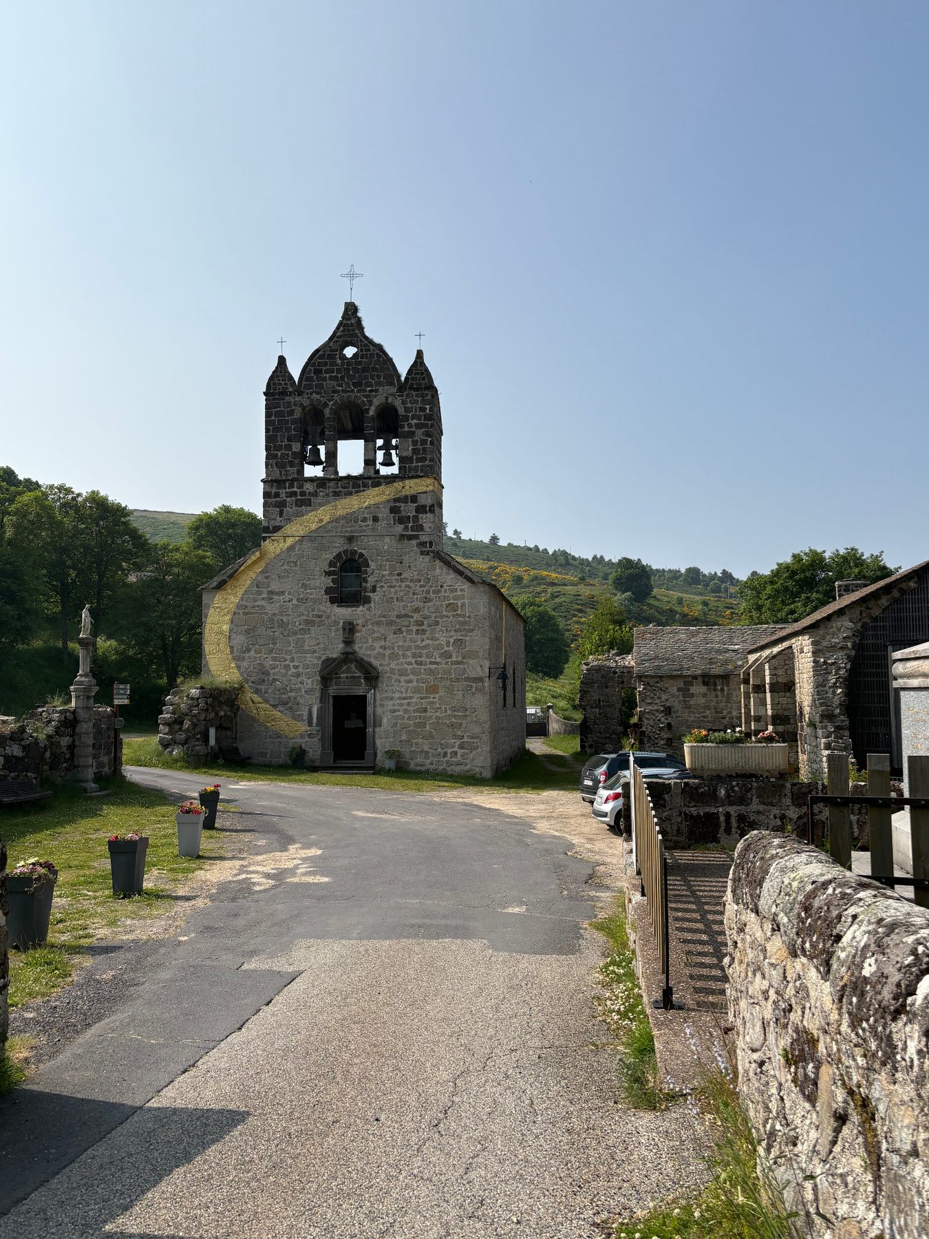 Église de Mazan-l'Abbaye et son clocher-mur à trois cloches, façade barrée d'un large tracé doré en arc de cercle