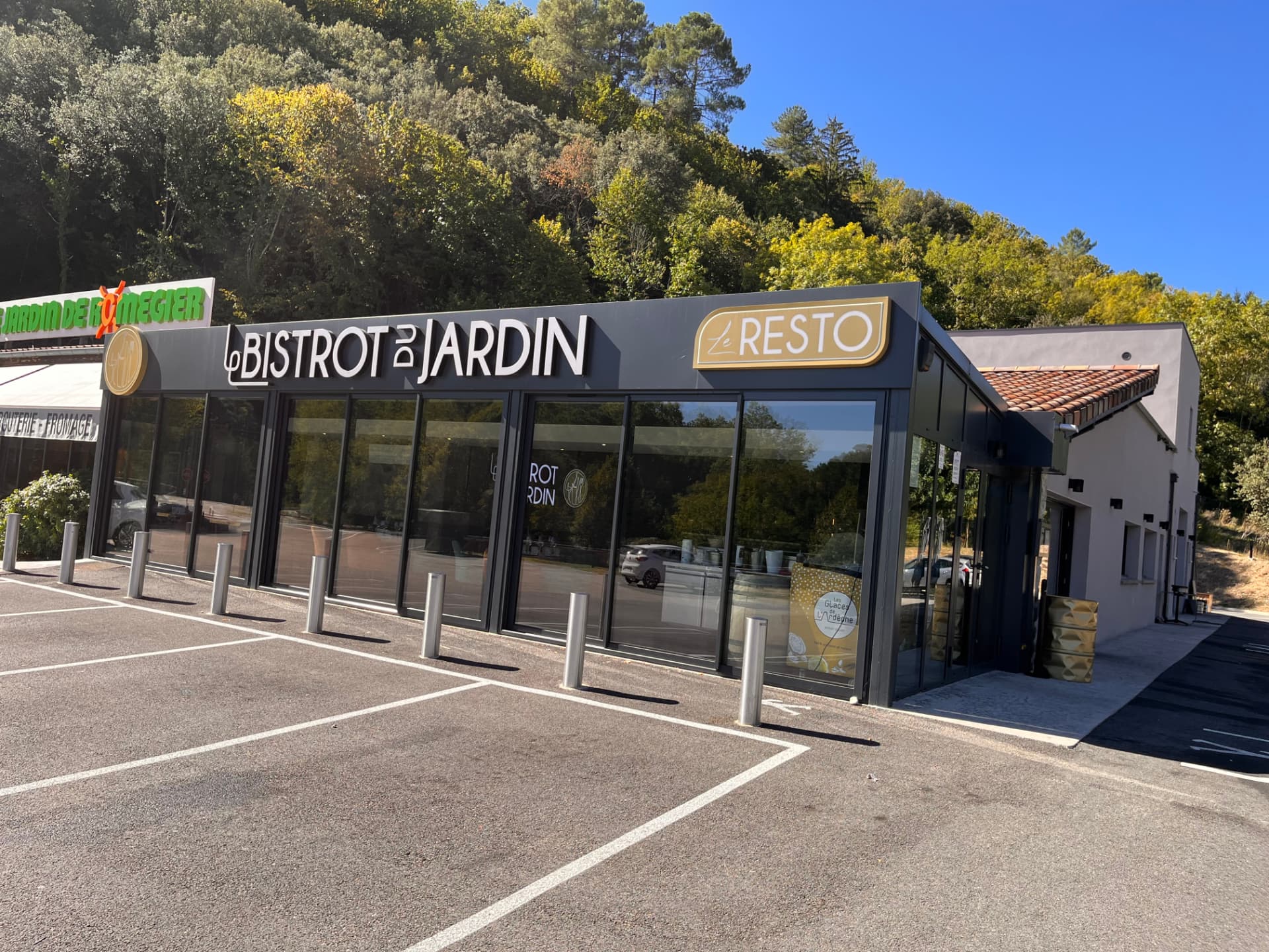 Façade principale du Bistrot du Jardin vue depuis le parking, enseignes du restaurant au-dessus des grandes vitres