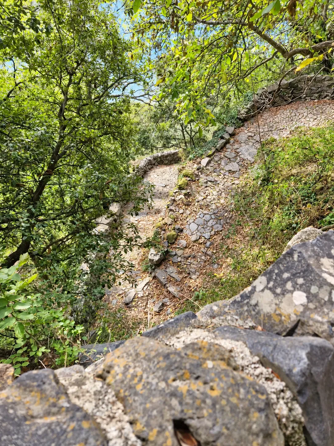 Sentier pavé de pierres qui serpente en lacet entre des murets, vu depuis un rocher